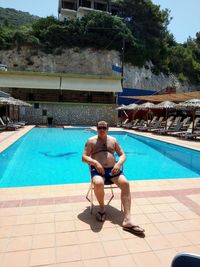 Full length of shirtless man sitting in swimming pool