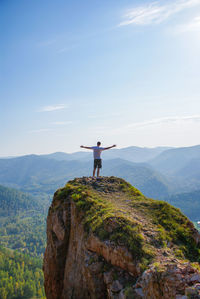 Man standing on rock by mountain against sky