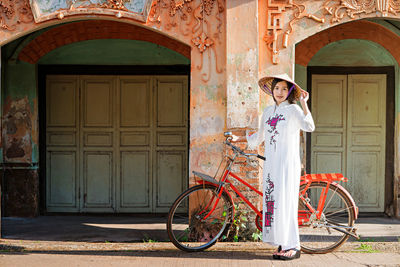 Portrait of young woman with bicycle standing against closed building door