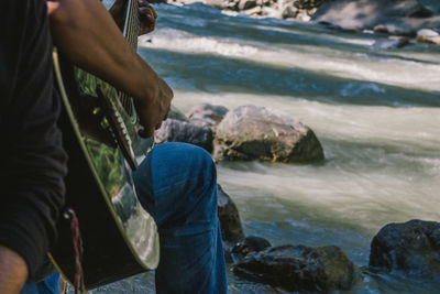 Midsection of guitarist with friend at riverbank