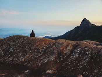 Rear view of people sitting on rock against sky during sunset