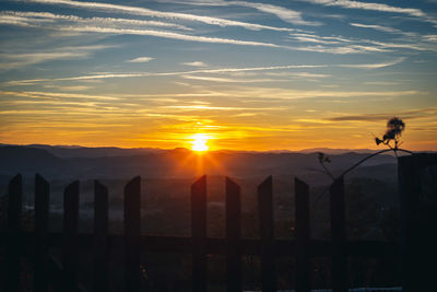 Silhouette wooden posts on landscape against sky during sunset