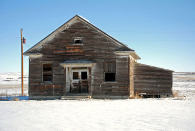 Abandoned house on snow covered field against sky