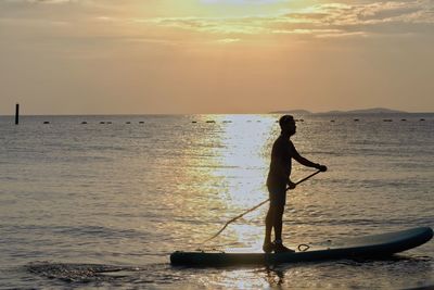 Silhouette man standing in sea against sky during sunset