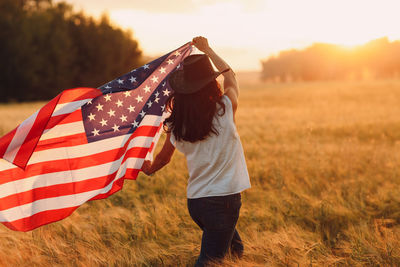 Rear view of woman holding american flag on field