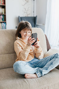 Girl schoolgirl plays mobile phone sitting on the couch. young blogger. social media