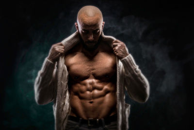 Bald muscular man standing against black background