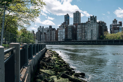 Modern buildings by river against sky in city