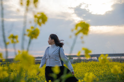 Woman standing by yellow flowers on field