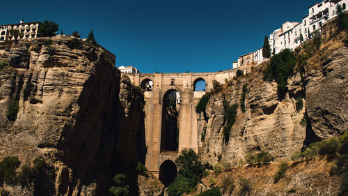 Low angle view of puente nuevo bridge amidst mountains against clear sky