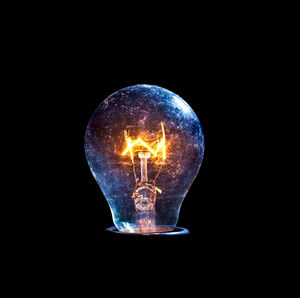 Close-up of illuminated light bulb against black background