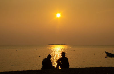 Silhouette people on sea against sky during sunset