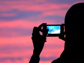 Close-up of woman photographing through smart phone against sunset sky