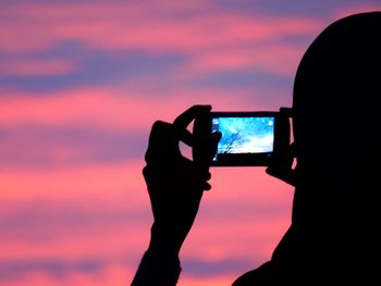 Close-up of man photographing through smart phone against sunset sky