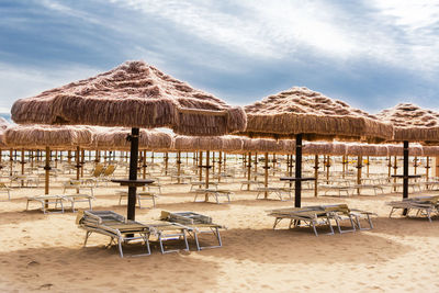 Lounge chairs and tables on beach against sky