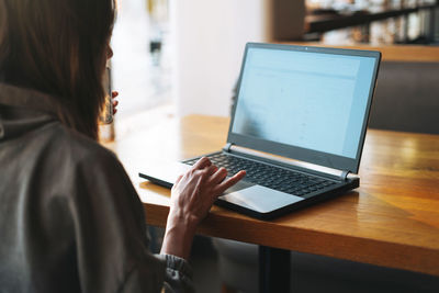 Young brunette woman in casual clothes working with laptop using mobile phone at cafe