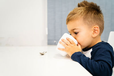 Boy having drink in cup while sitting at table