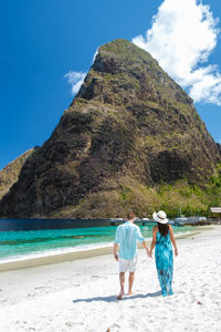 Rear view of woman walking at beach against sky