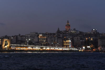Illuminated buildings by sea against sky at night