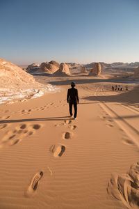 Full length rear view of man walking in desert against clear sky