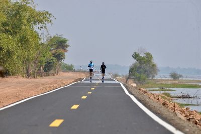 Rear view of people walking on road against clear sky