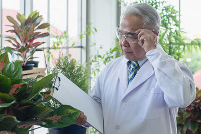 Man wearing mask holding while standing against plants