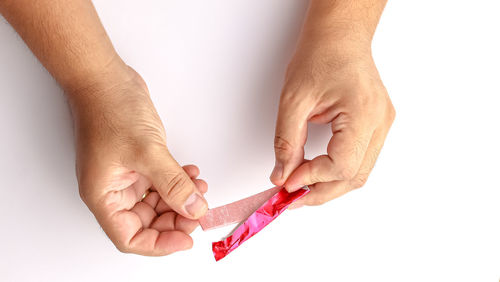 Cropped hands of man cutting chewing gum against white background