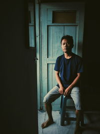 Young man looking away while sitting on door of building