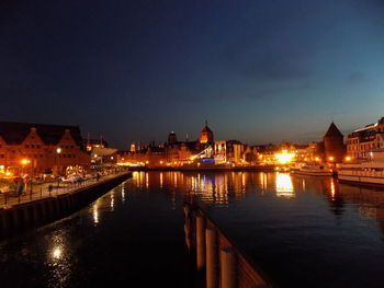 Illuminated buildings by river against sky at night