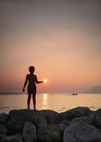 Full length of man standing on rock at beach during sunset