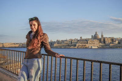 Young woman standing by railing against river