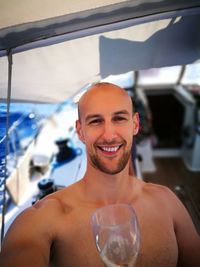 Portrait of shirtless man holding wineglass while standing in boat