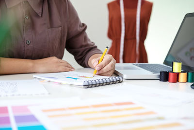 Midsection of female fashion designer drawing on book at desk