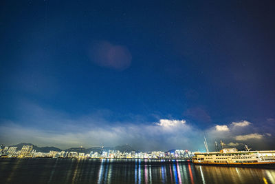 Illuminated city by sea against sky at night