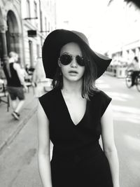 Portrait of young woman wearing sunglasses standing on street in city