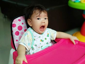 Portrait of cute baby girl sitting on pink high chair