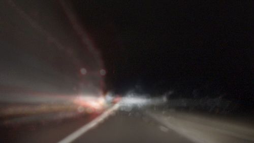 Defocused image of illuminated road against sky at night