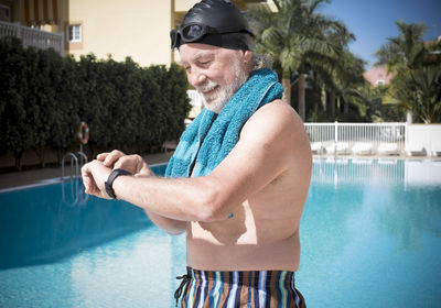 Shirtless man checking time while standing against pool