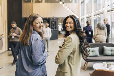 Portrait of smiling female entrepreneurs looking over shoulder while standing at convention center