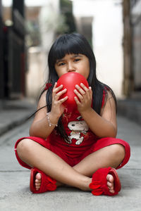 Portrait of girl holding ball while sitting outdoors