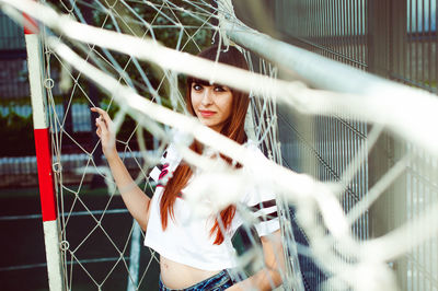 Portrait of young woman standing at soccer goal post