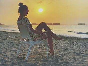 Woman sitting on chair at beach during sunset