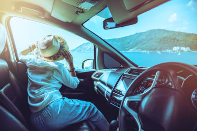 Rear view of woman looking at sea through car window