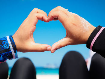 Midsection of man holding heart shape against blue sky
