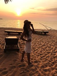 Full length of woman standing on beach against sky during sunset
