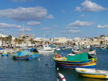 Sailboats moored on harbor by city against sky