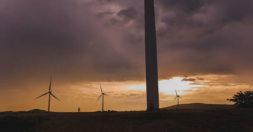 Silhouette wind turbines on field against sky during sunset