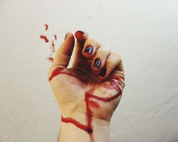 Cropped image of woman hand covered with blood against wall