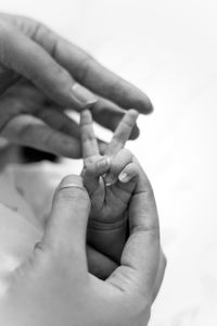 Cropped hands of mother holding baby hand against white background