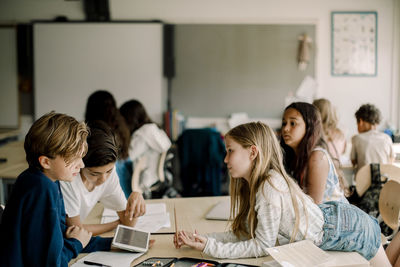 Female student leaning over table while friends sitting in classroom